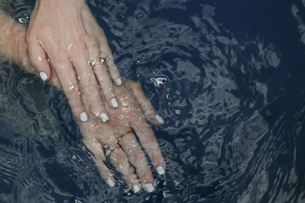 Obrázek ženských rukou s bílým lakem na nehty v modré vodě - Fotografie, Obrázek