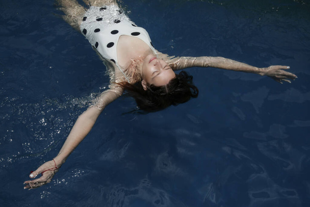 Retrato franco ao ar livre de jovem mulher em bolinhas swimwear desfrutando de dia quente de verão flutuando em água fria piscina azul. Conceito férias de verão
. - Foto, Imagem