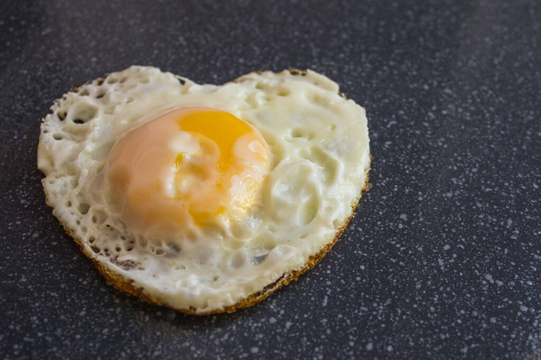 Un uovo solo fritto in una padella a forma di cuore. Ucciso dall'amore, bruciato. Amore bruciato. Sfondo scuro
. - Foto, immagini