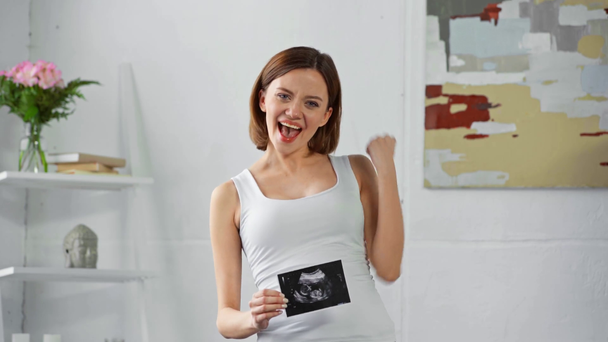 Mujer embarazada alegre con ecografía del bebé mostrando sí
 - Metraje, vídeo