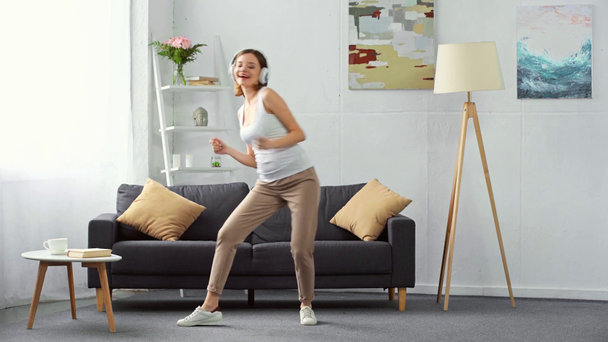 Felice donna incinta in cuffia ballare con smartphone a casa
  - Filmati, video