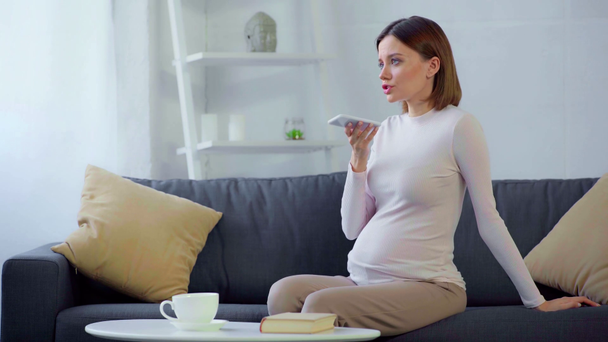 Těhotná žena pomocí smartphone na gauči  - Záběry, video