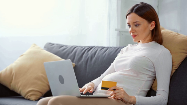 Ragazza incinta sorridente con carta di credito e laptop sul divano
 - Filmati, video