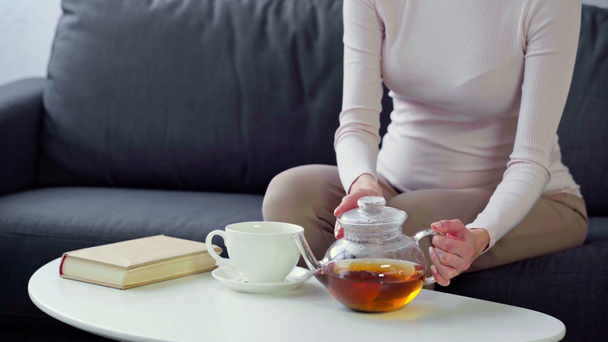Vue recadrée de la femme enceinte buvant du thé près du livre sur la table basse
 - Séquence, vidéo