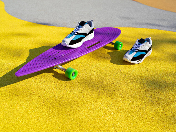 Napfényes színes jelenet tornacipők és lila longboard. - Fotó, kép