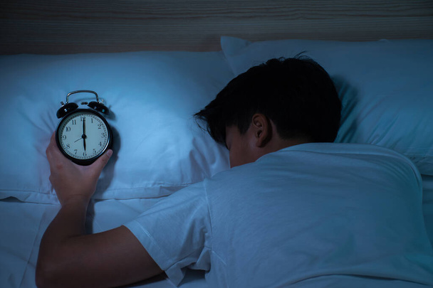 Os asiáticos usam camisetas brancas, dormindo e segurando seus relógios na cama depois de trabalhar duro do trabalho
. - Foto, Imagem