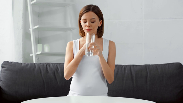 Terhes nő vesz tablettát vízzel a kanapén otthon  - Felvétel, videó