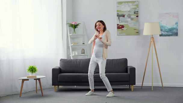 Χαρούμενη έγκυος γυναίκα που χορεύει στο σαλόνι - Πλάνα, βίντεο