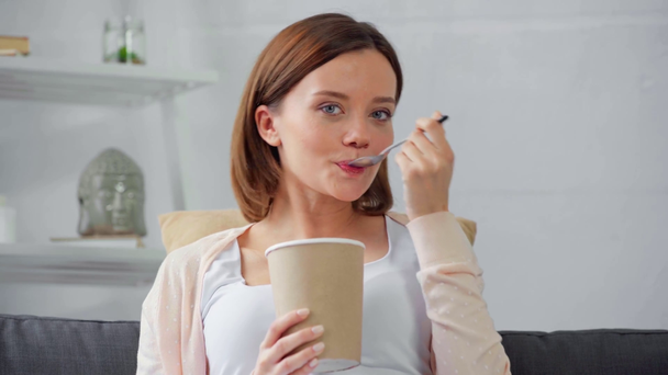 Mosolygó nő eszik jégkrémet a kanapén  - Felvétel, videó