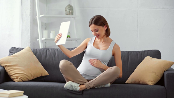 Boldog terhes lány, amelynek videohívás digitális tabletta kanapén  - Felvétel, videó