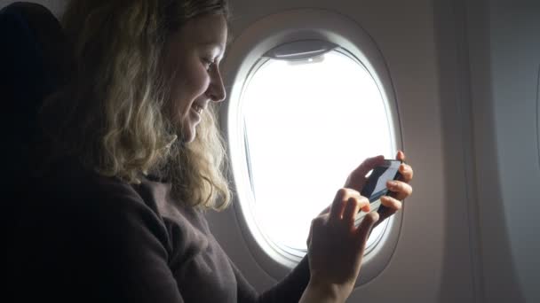 girl sits by airplane window and looks at photos on phone - Video