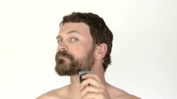 Ein Mann im Studio, der ein Rasiermesser in der Hand hält, beginnt, sich den Bart abzurasieren. Aufgenommen in 4K. - Filmmaterial, Video