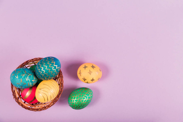 Кольорові великодні яйця в дерев'яному кошику на фіолетовому тлі. Вид зверху
 - Фото, зображення
