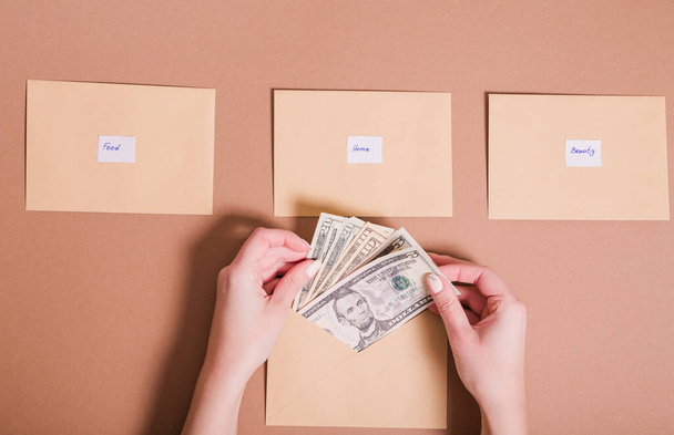 Dollars in female hands and envelopes with inscriptions for saving money on a brown background. Money saving concept - Photo, Image