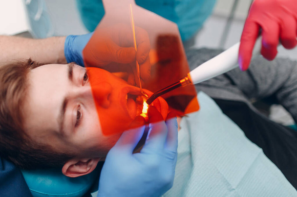 Odontologia. Dentista e paciente. Selo de cura leve. Lâmpada dental UV e laranja proteger vidro
. - Foto, Imagem
