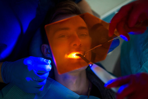 Οδοντιατρική. Οδοντίατρος και ασθενής. Ελαφρύ σφράγισμα. UV οδοντιατρική λάμπα και πορτοκαλί προστατευτικό γυαλί. Οδοντιατρικές σφραγίσεις. - Φωτογραφία, εικόνα