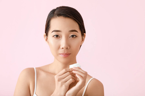 Hermosa joven mujer asiática con crema sobre fondo de color - Foto, Imagen