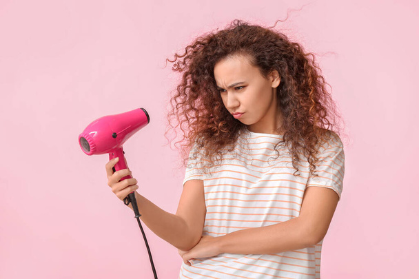 Frowning young woman with blow dryer on color background - Photo, Image