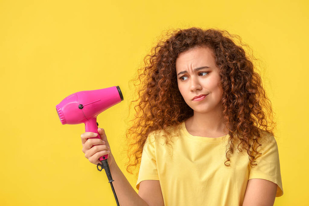 Beautiful confused African-American woman with blow dryer on color background - Photo, Image