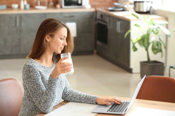 Bella giovane donna con computer portatile bere latte a casa
 - Foto, immagini