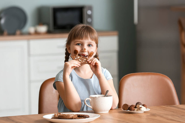 schattig klein meisje eten chocolade in keuken - Foto, afbeelding