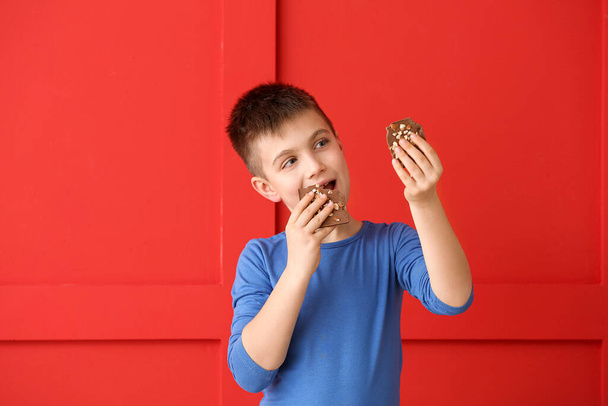 Cute little boy eating chocolate on color background - Photo, Image