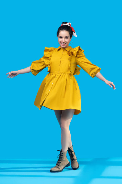 Young woman in a mustard dress standing with legs crossed - Foto, imagen