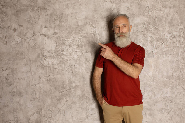 Presenting your product. Confident senior man in casual wear pointing away and looking at camera while standing against grey background. - Fotografie, Obrázek