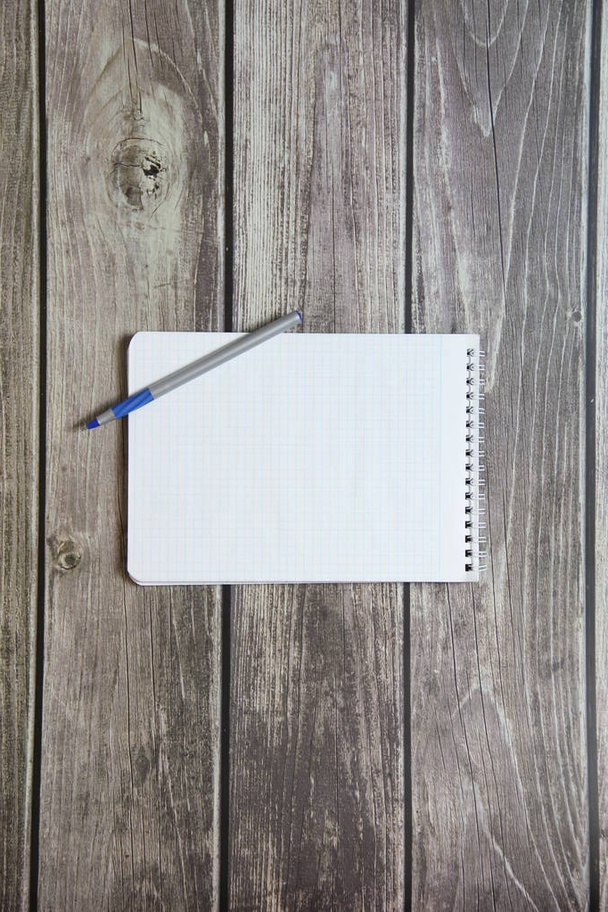 Notepad with a blank white sheet in a checker paper with ball pen lies on the background of wooden boards. - Valokuva, kuva