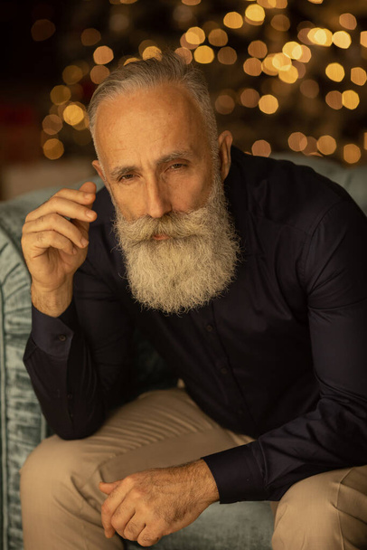 Positive elderly bearded gentleman smiling looking at camera sitting on sofa at home. - Fotoğraf, Görsel