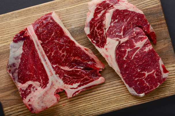 Fresh raw beef steak on wooden cutting board, top view. Served over black background. - Foto, Bild