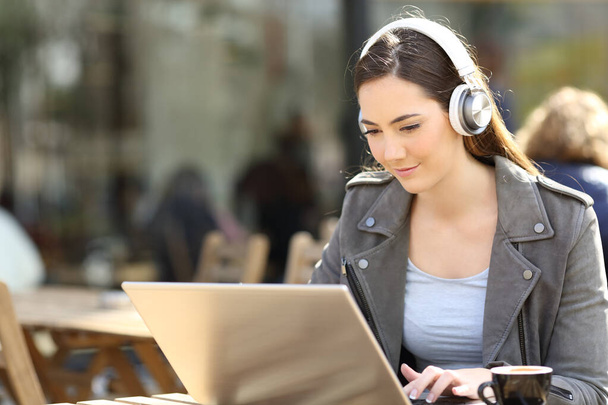 Concentrated girl watching media content on laptop with headphones on a cafe terrace - Foto, Imagem