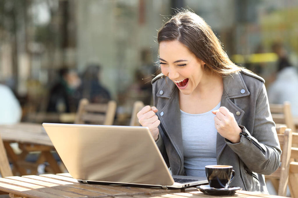 Excited woman reading good news on laptop sitting in a coffee shop terrace - Foto, Bild