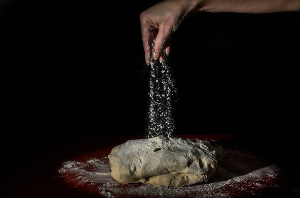 Chef sprinkles raw dough with white flour on a black background - 写真・画像