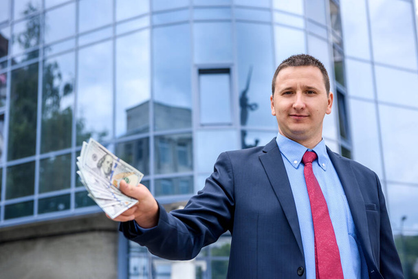 Νεαρός άνδρας με χαρτονομίσματα του δολαρίου στέκεται κοντά στο επιχειρηματικό κέντρο - Φωτογραφία, εικόνα