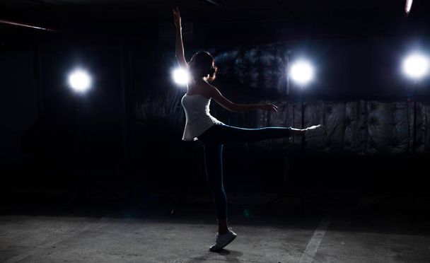 Asiático magro Fitness mulher exercício aquecimento balé dança estiramento corpo braço pernas salto em branco camisa jean calças fumaça escuro fundo ambiente, estúdio iluminação aro de volta luz baixa exposição cópia espaço
 - Foto, Imagem