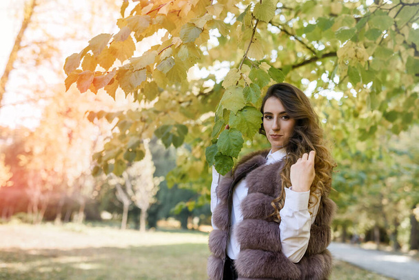 Woman wearing fashionable fur coat walking in autumn park. - Foto, afbeelding