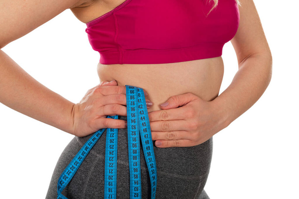 Cintura de las hembras jóvenes, sosteniendo una cinta métrica sobre un fondo aislado: pérdida de peso, dieta, concepto de conformación corporal
 - Foto, imagen