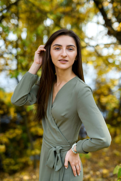 Portrait of brunette woman in green dress posing in autumn park - Фото, изображение