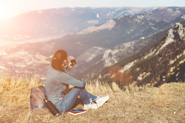 Zpětný pohled na cestování žen. Mladá krásná dívka cestuje sama v horách na jaře nebo na podzim, sedí na okraji hory a dívá se do dálky - Fotografie, Obrázek