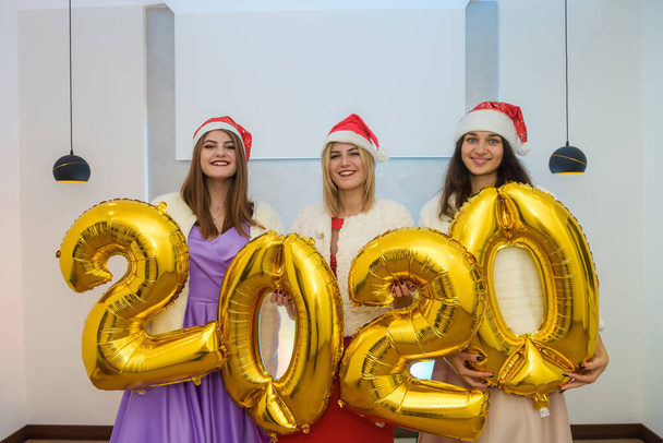 Tres alegres mujeres con globo aerostático dorado posando en elegantes vestidos de noche. Celebración del año nuevo
 - Foto, imagen