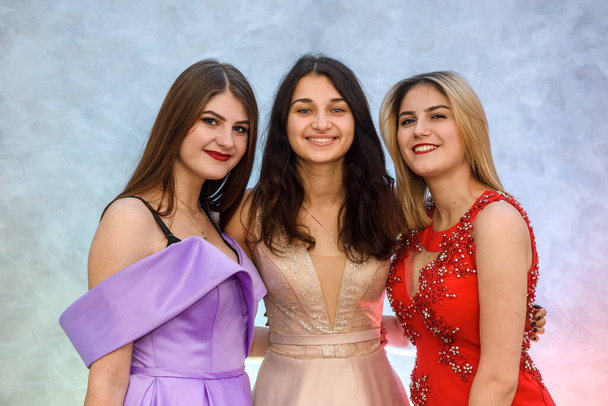 Tres chicas felices en vestidos elegantes posando sobre fondo abstracto. Concepto de celebración
 - Foto, imagen