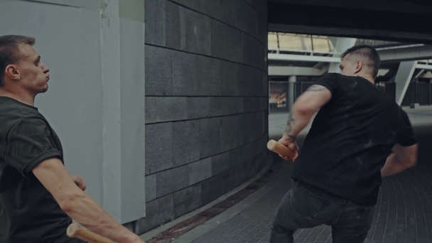wysportowani mężczyźni z kijami bejsbolowymi walczący na ulicy - Materiał filmowy, wideo