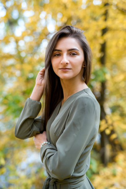 Porträt einer brünetten Frau in grünem Kleid posiert im Herbstpark - Foto, Bild
