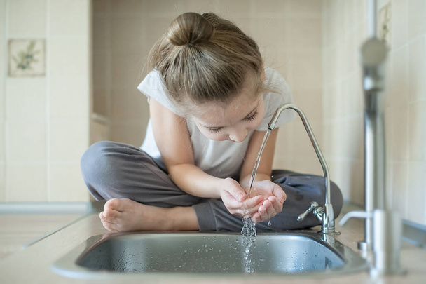 Caucasian little girl drinking from water tap or faucet in kitchen. Hands open for drinking tap water. Pouring fresh healthy drink. Good habit. Right choice. Environment concept. World Water Day - Photo, image
