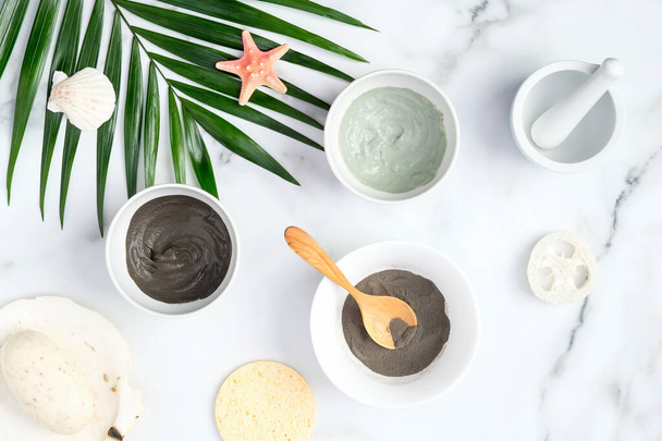 SPA natural organic facial clay mask and powder in bowls and tropical palm leaf on marble desk. Beauty products for face skin care and treatment concept. - Fotó, kép