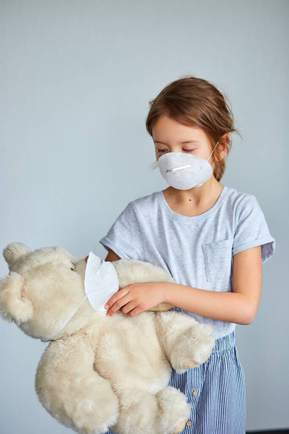 Little girl holding and hugging teddy bear in mask. Coronavirus, covid-19 and pollution protection concept. Stay at home. - Valokuva, kuva