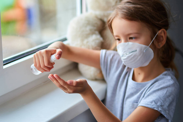 Mała dziewczynka nosi maskę higieniczną i wciska spray alkoholowy, by chronić, odkażać. Koncepcja koronawirusa, wideowirusa-19 i ochrony przed zanieczyszczeniami. Zostań w domu.. - Zdjęcie, obraz