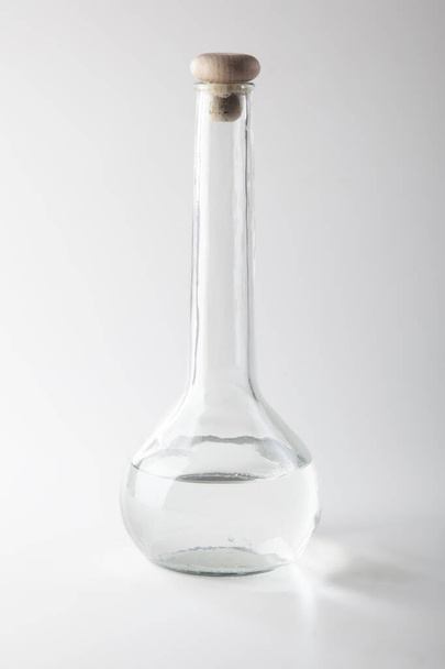 studio shot of bottle with long neck with wooden stopper and clear liquid on light grey background - Zdjęcie, obraz