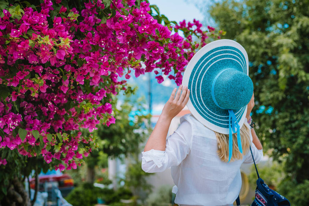 Elegant dressed woman with hat smelling beautiful colorful flowers on the islands of Greece during summer time. Romantic Traveling vacation concept - Fotografie, Obrázek